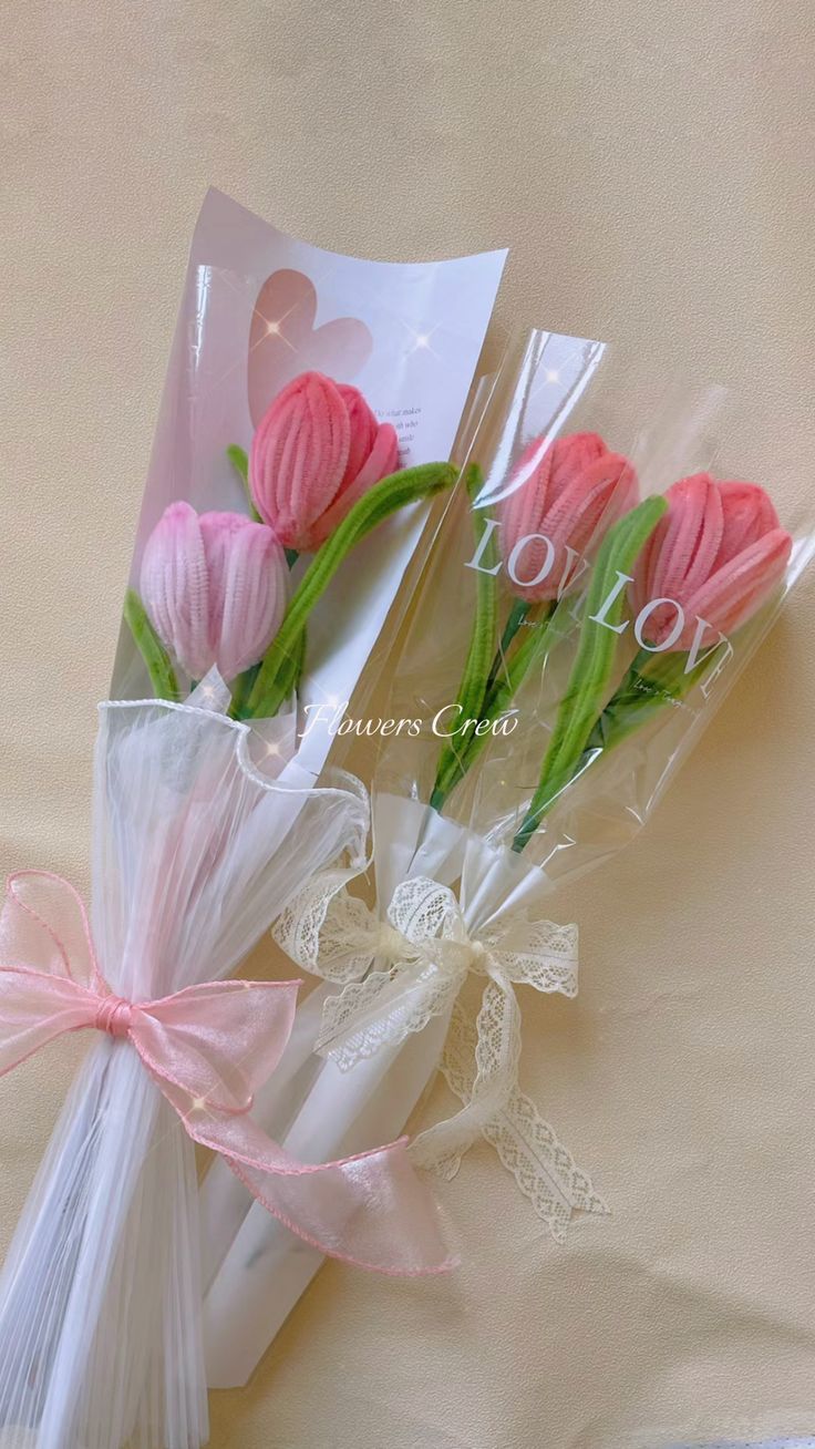 three pink tulips wrapped in cellophane and tied with ribbon on a bed