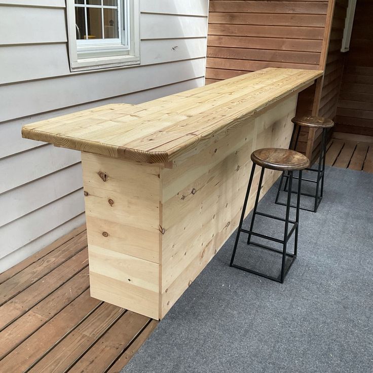 two stools sitting next to a wooden bar on a porch with a house in the background