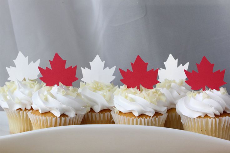 four cupcakes with white frosting and red maple leaves on top are sitting on a plate