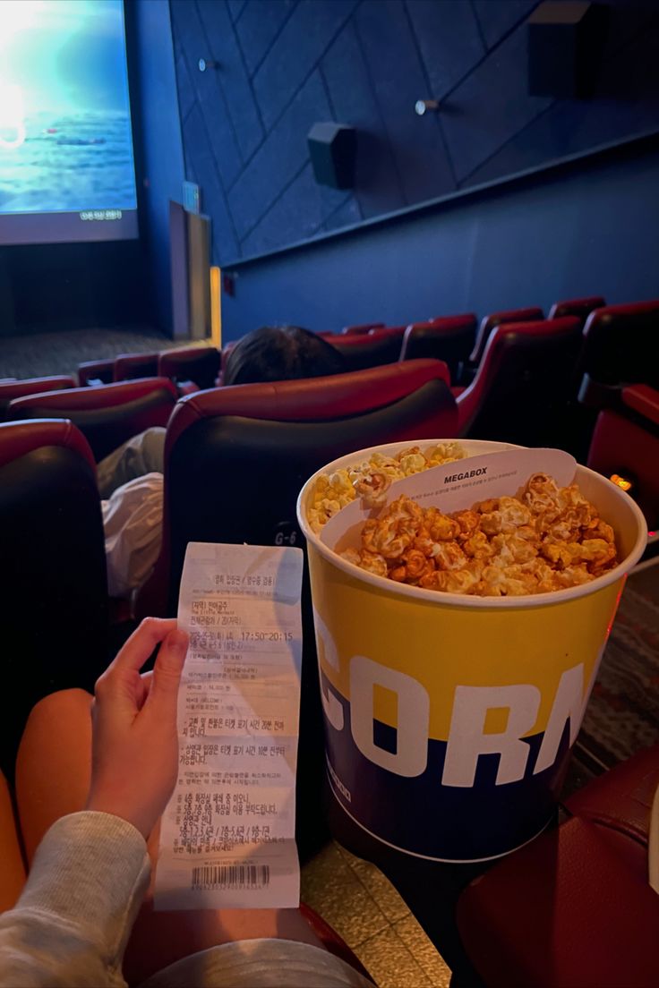 a person sitting in front of a movie screen with a bucket of popcorn next to it