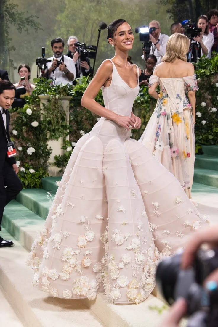 a model walks down the runway in a white gown with flowers on it and people taking pictures