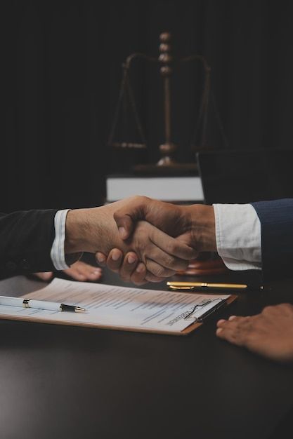 two people shaking hands at a table with papers and a judge's scale in the background