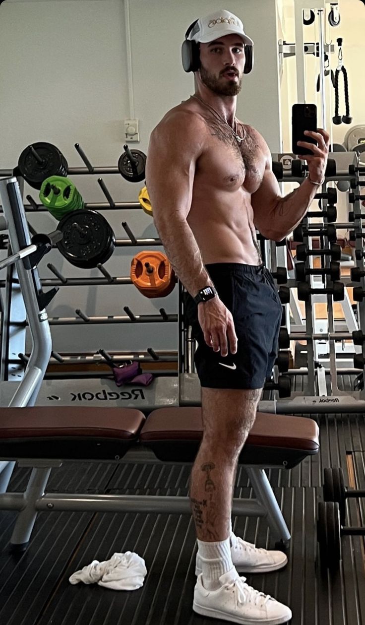 a shirtless man taking a selfie with his cell phone in the middle of a gym