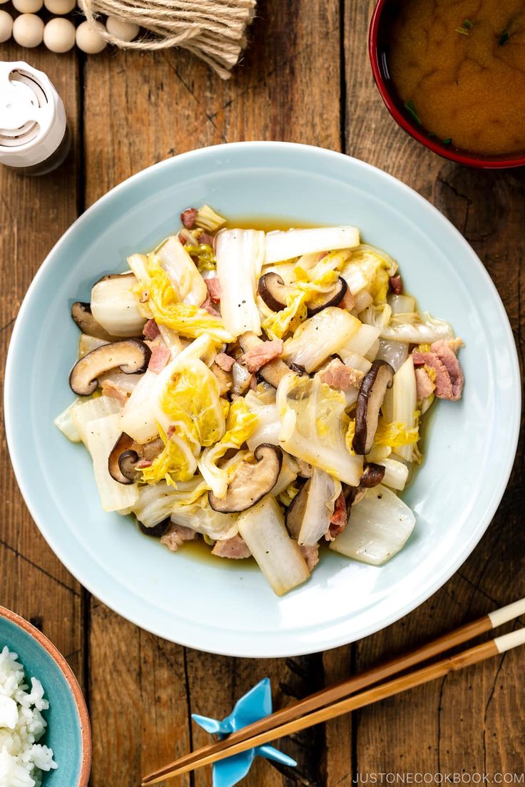 a white plate topped with food next to chopsticks and a bowl of rice