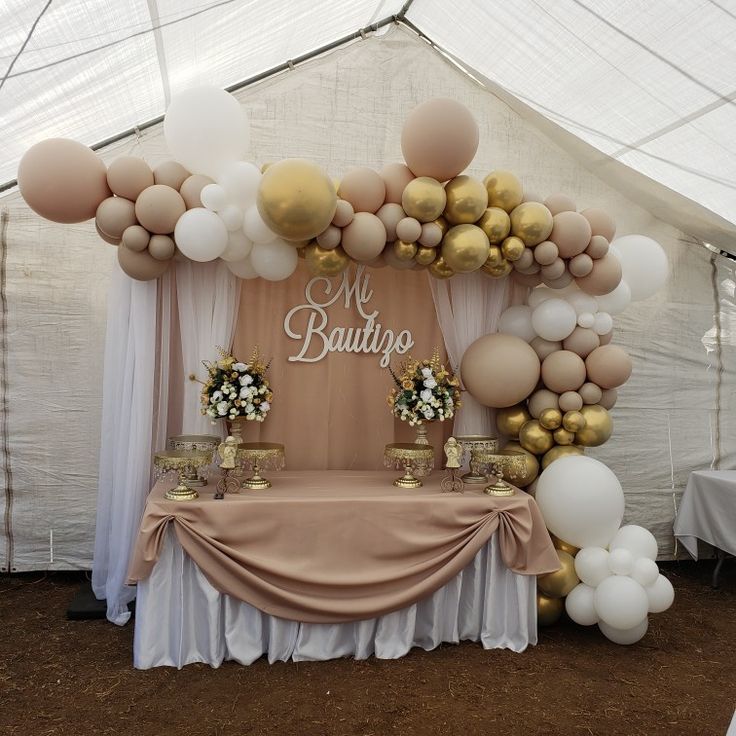 a table topped with lots of balloons next to a white and gold tented area