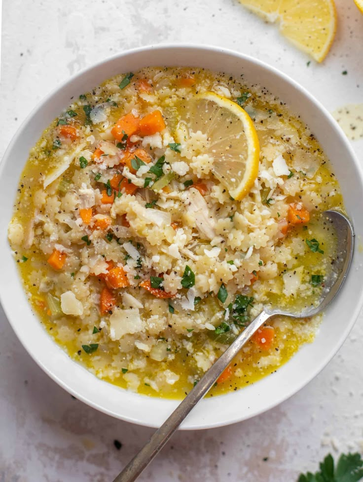 a white bowl filled with soup next to sliced lemons and parmesan cheese