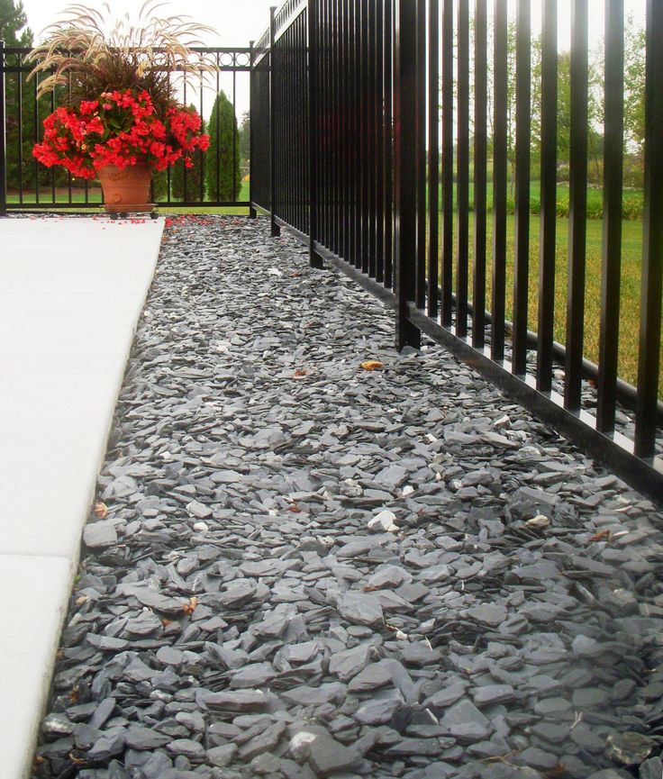 a black iron fence next to a flower pot with red flowers in it and gravel on the ground