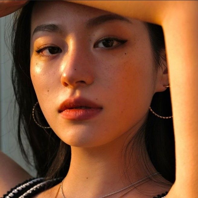 a close up of a person wearing necklaces and holding her hand on her head