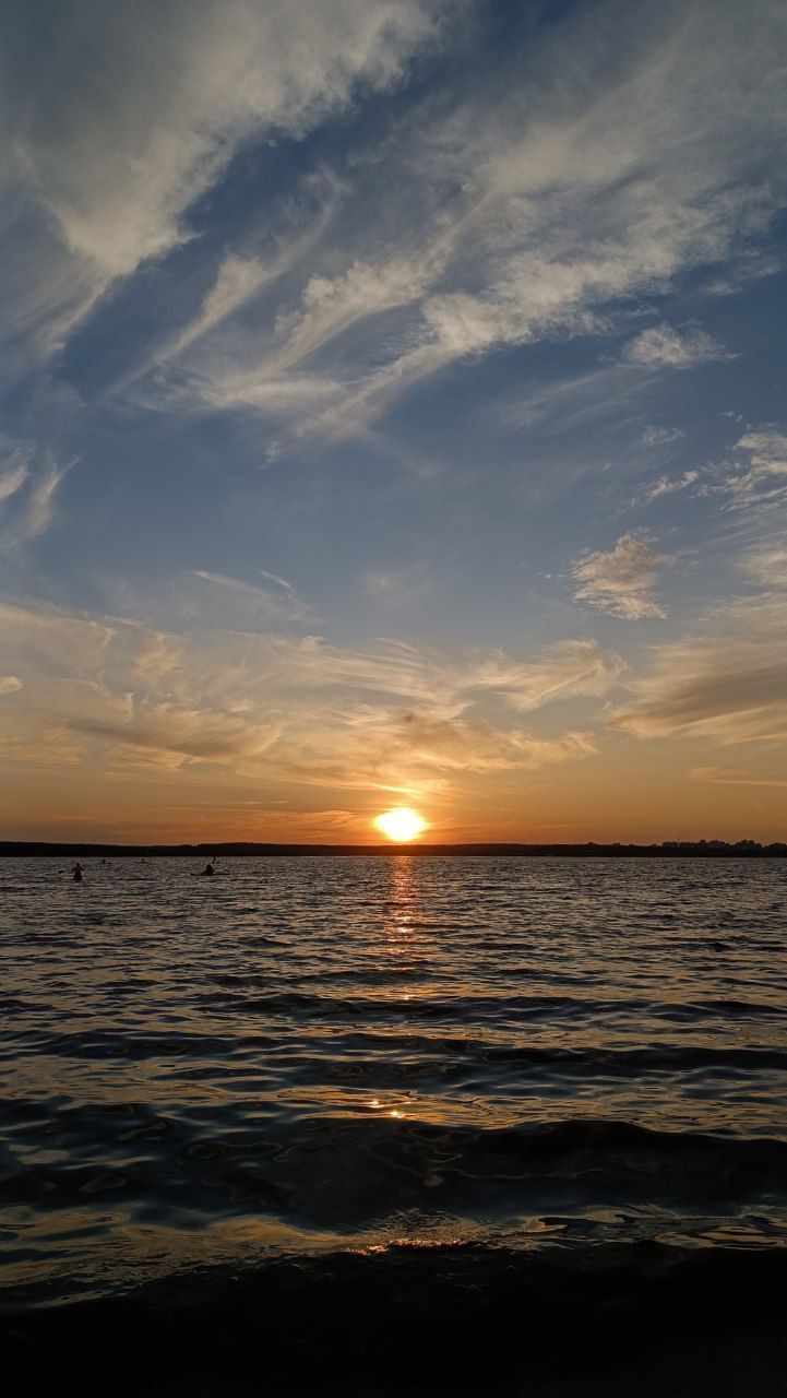 the sun is setting over the ocean with some clouds in the sky and boats out on the water