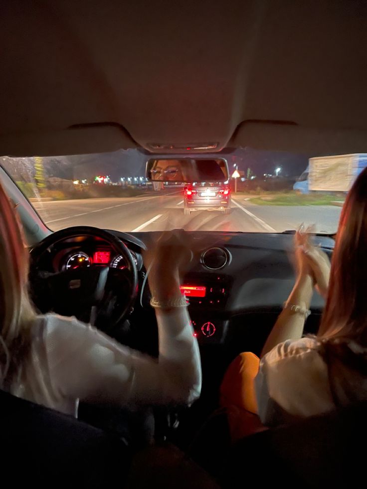 two women in the drivers seat of a car driving down a highway at night time