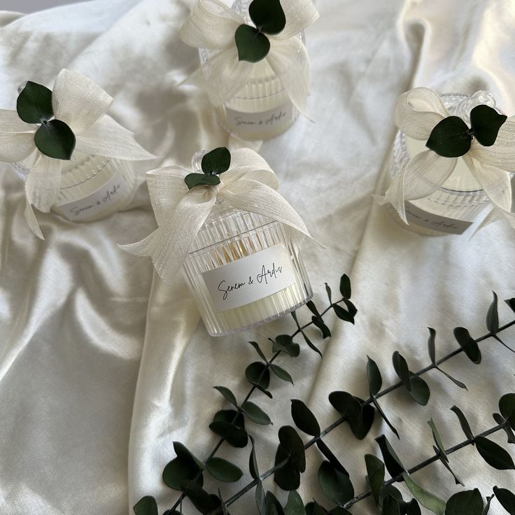 three small bottles with white flowers in them on a table cloth next to some green leaves