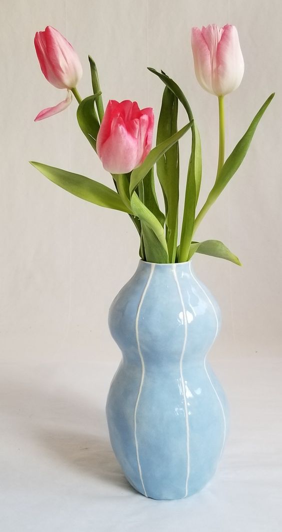 three pink tulips in a blue vase on a white tableclothed background