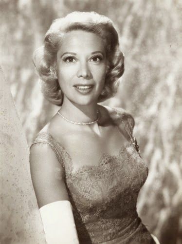 an old black and white photo of a woman in a dress posing for the camera