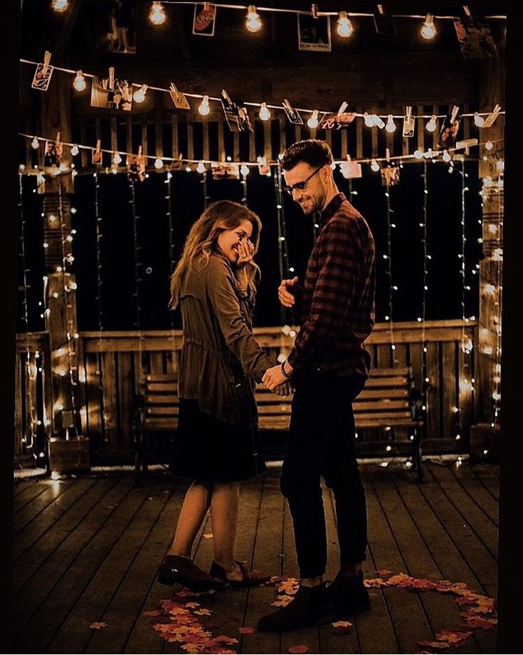 a man and woman are standing on a deck with string lights strung across the room