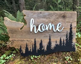 a wooden sign with the word home painted on it in front of trees and bushes