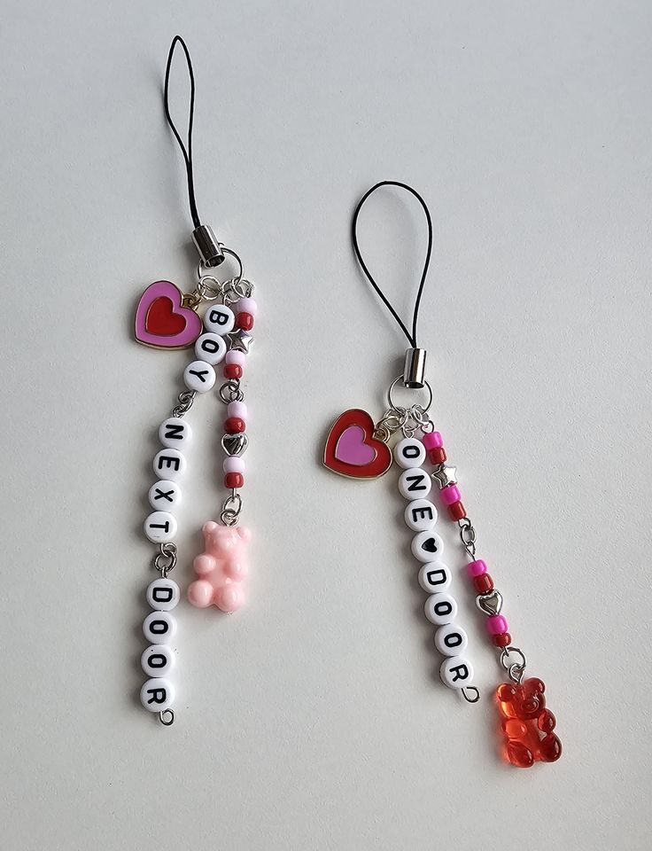 two necklaces with hearts and words hanging from strings on a white surface, one has a red heart in the middle