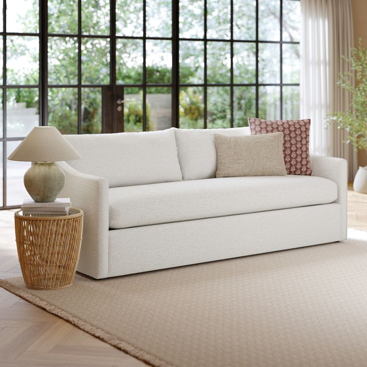 a white couch sitting on top of a wooden floor next to a table with a lamp