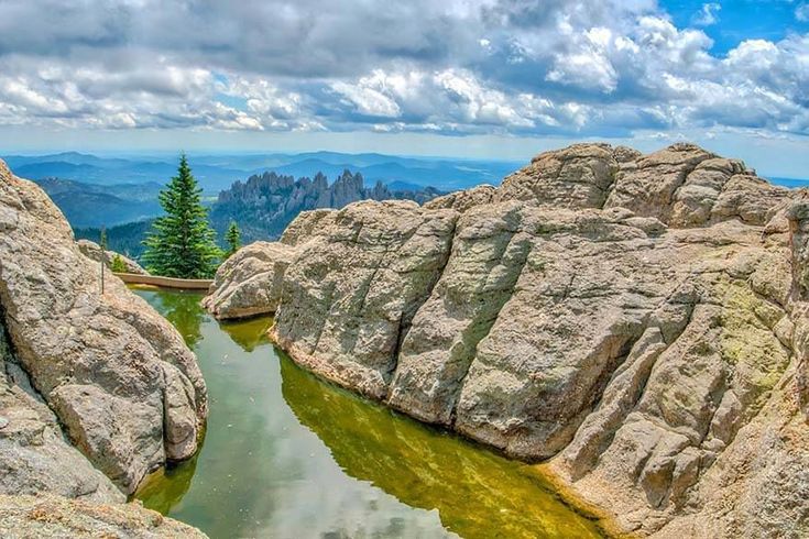 some rocks water and trees on a cloudy day at the top of a rock formation