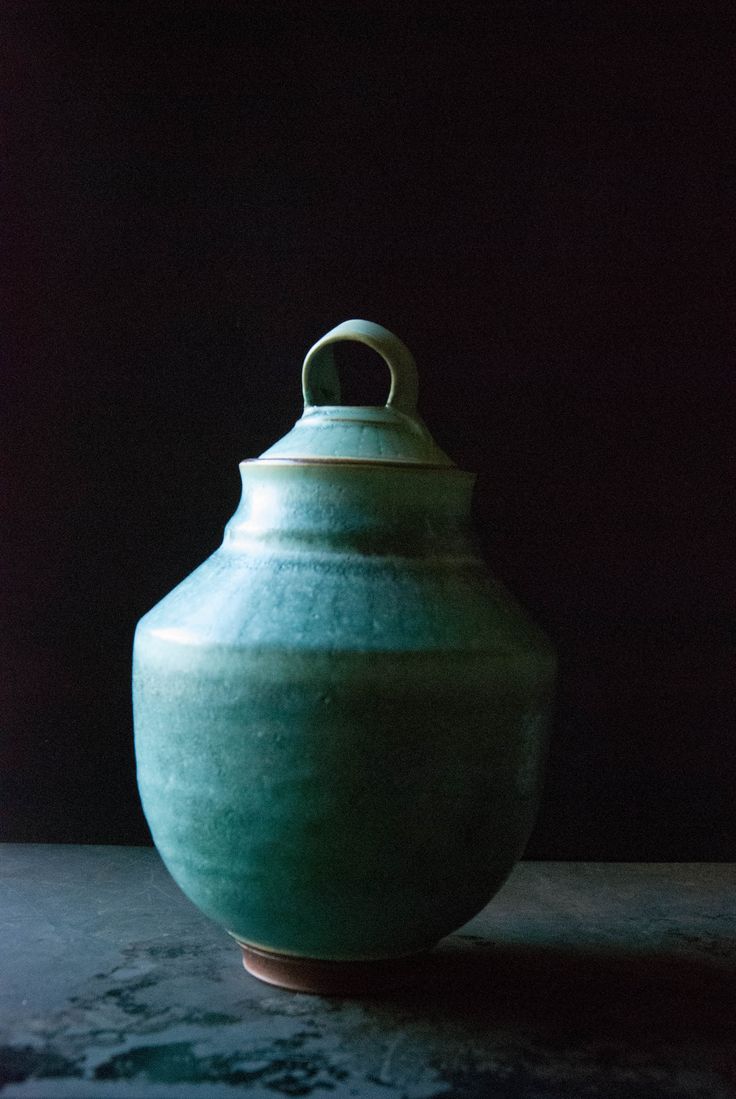 a green vase sitting on top of a table next to a black wall and floor