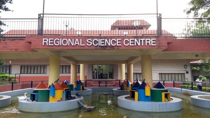 the front entrance to regional science centre with colorful sculptures in the water and people walking around