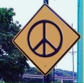 a yellow and black sign with a peace sign on it's side next to a blue pole