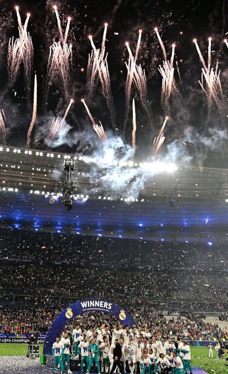 a group of people standing on top of a soccer field with fireworks in the air