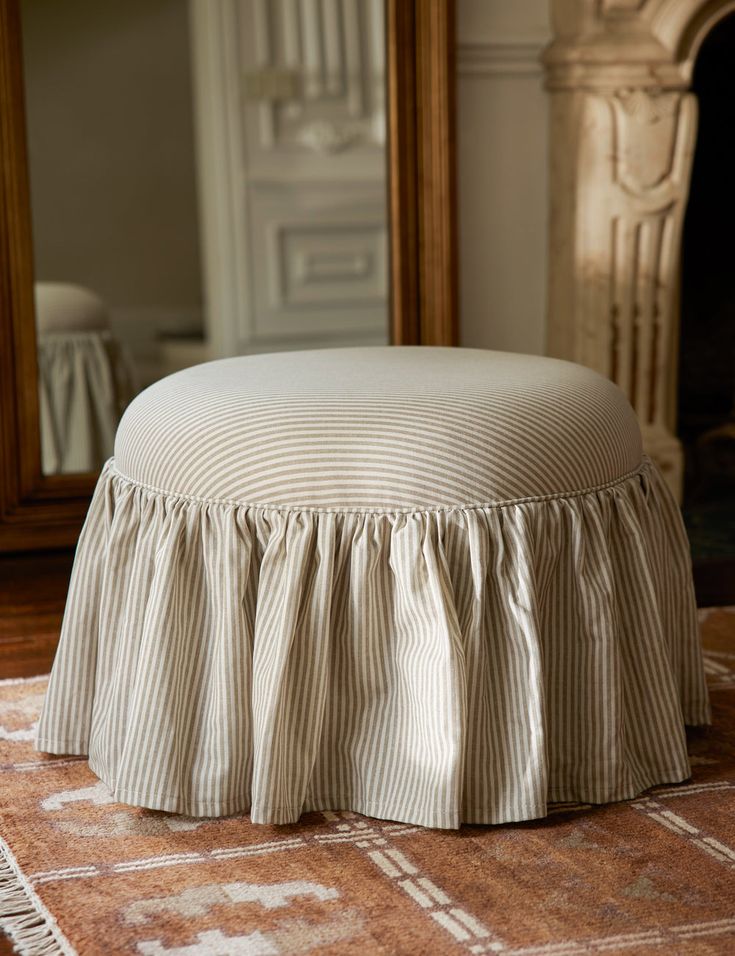 a round ottoman sitting on top of a rug in front of a mirror and fireplace