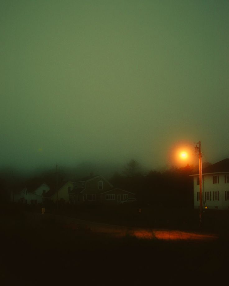 a foggy night with a street light in the foreground and houses in the background