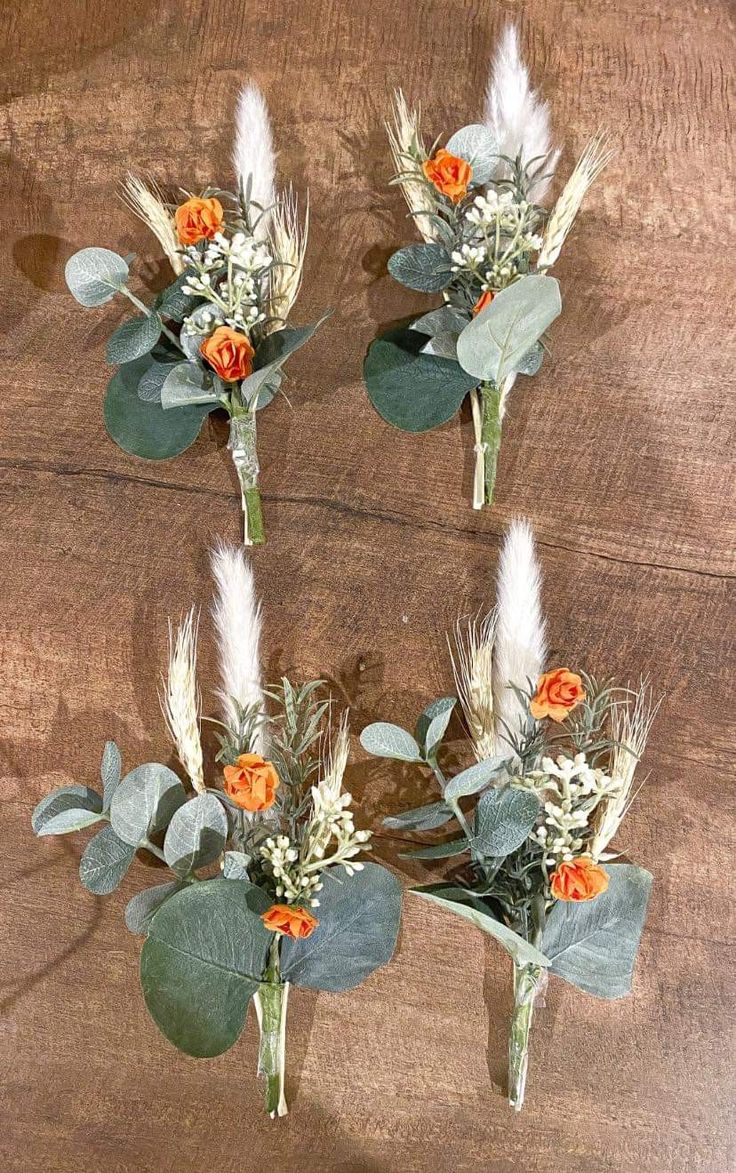 four boutonnieres with flowers and leaves on a wooden surface