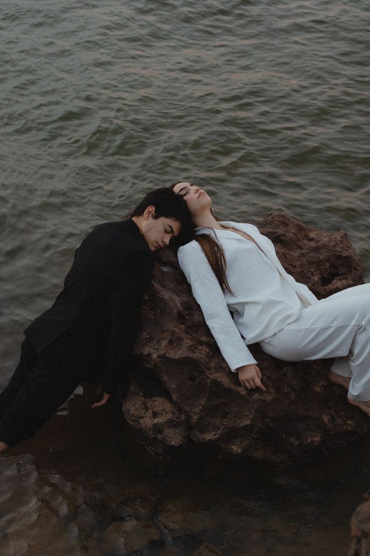 a woman laying on top of a rock in the water