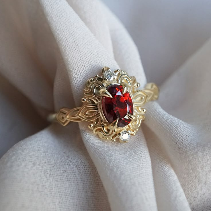 a close up of a ring with a red stone in it on a white cloth