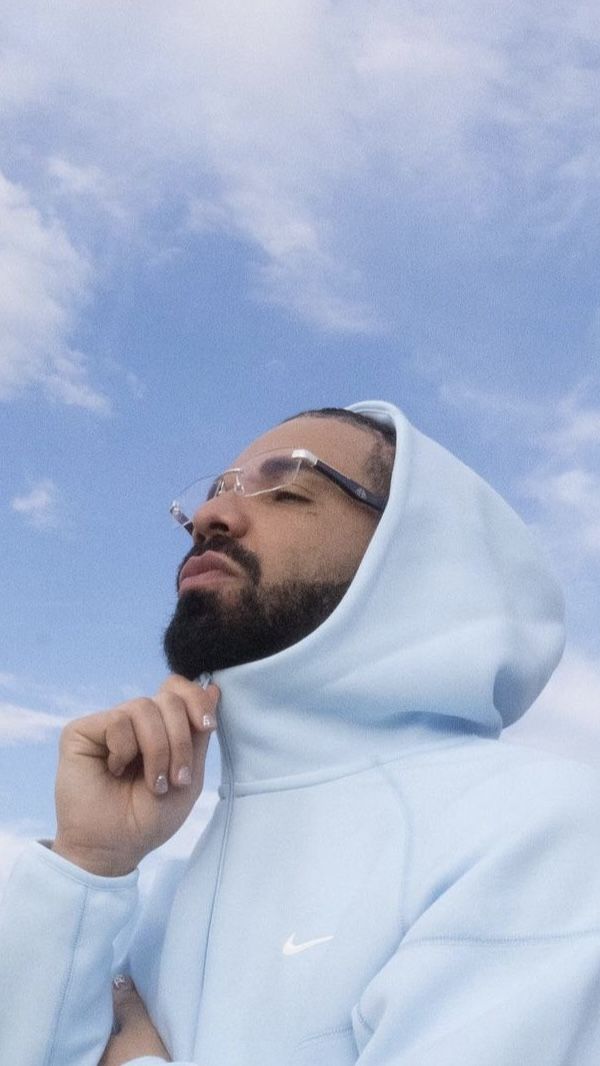 a man wearing glasses and a hoodie looks up into the sky while holding his hand under his chin