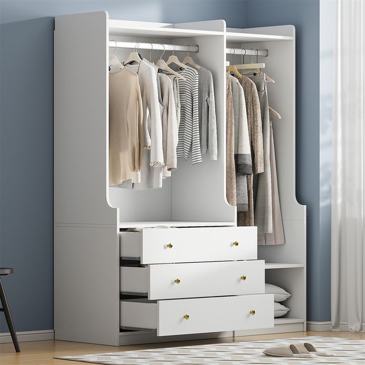 a white wardrobe with drawers and clothes hanging on it's doors, in a blue room