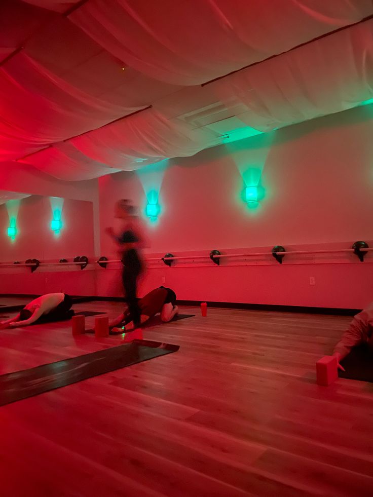 some people are doing yoga in a large room with red and green lights on the ceiling