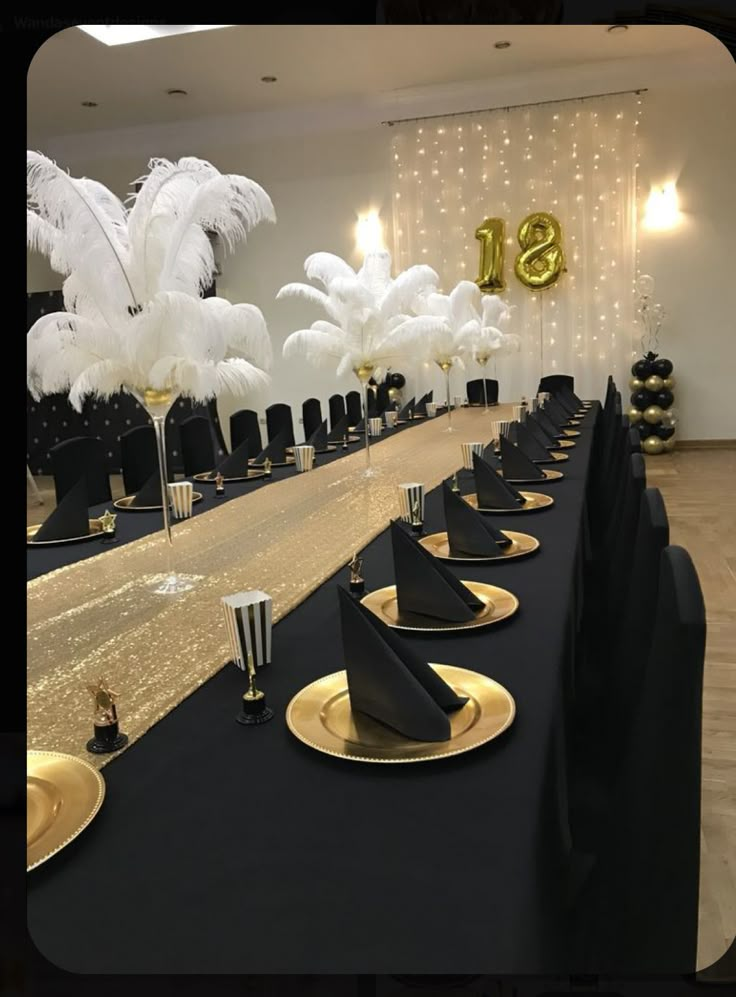 a long table with black and gold place settings, white feathers on the wall behind it