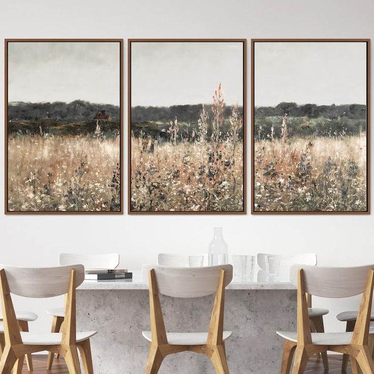 three paintings hanging on the wall above a dining room table with chairs and a vase