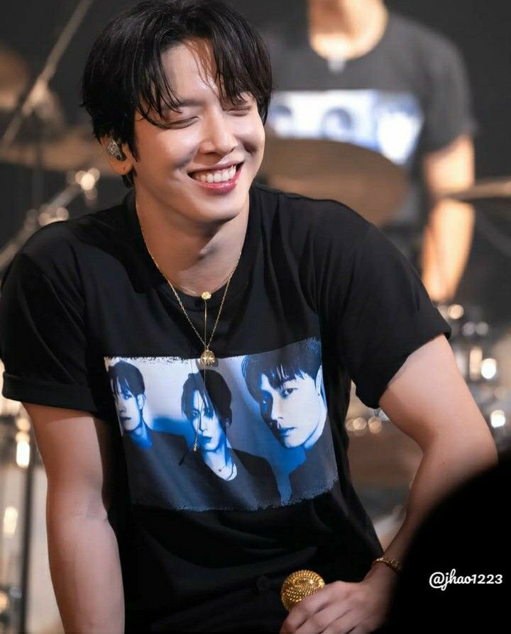 a young man sitting in front of a drum set smiling at the camera with his eyes closed