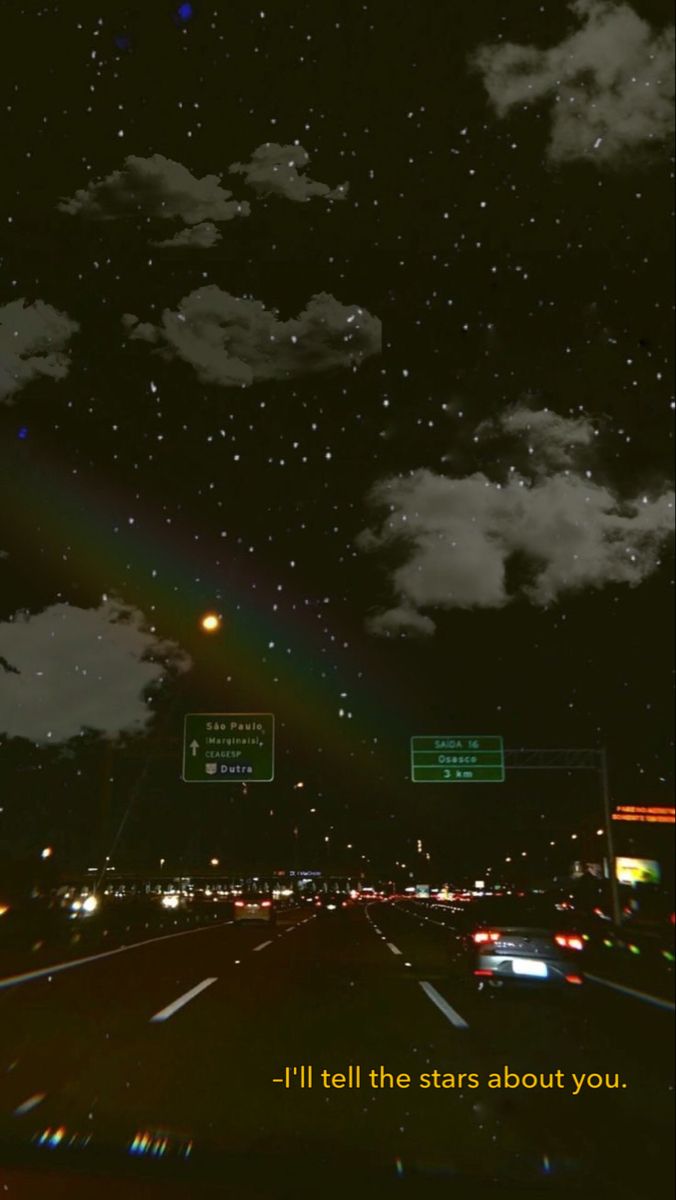 the sky is filled with clouds and stars as cars drive down the road at night