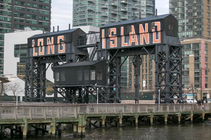 a large sign that reads long island on top of a bridge over water with tall buildings in the background