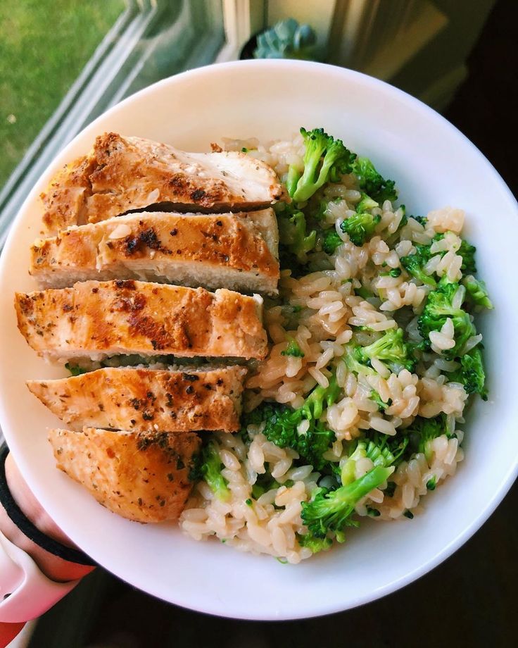 a person holding a plate with rice and broccoli on it, next to a window