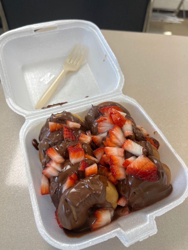 strawberries and chocolate in a plastic container with a fork on the table next to it