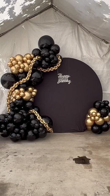 a black and gold balloon arch is set up in front of a white canvas tent