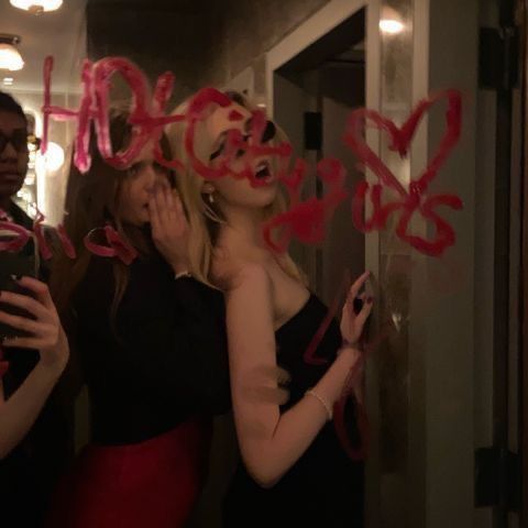 three women standing in front of a mirror with writing on it