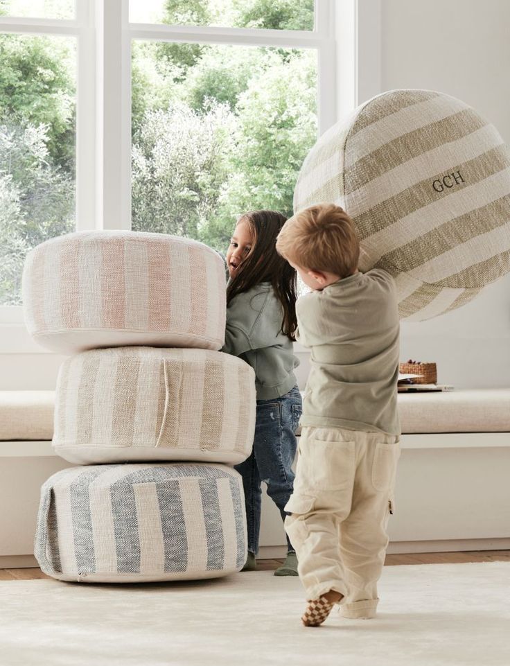 two children are playing with pillows in front of a window and another child is looking out the window