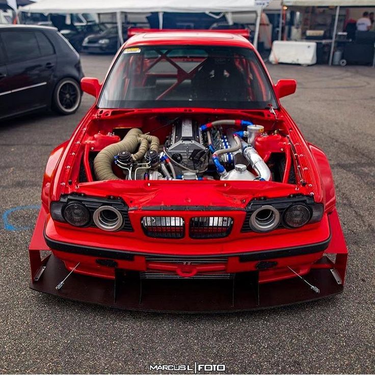 a red car parked in a parking lot with its hood up and engine bay open