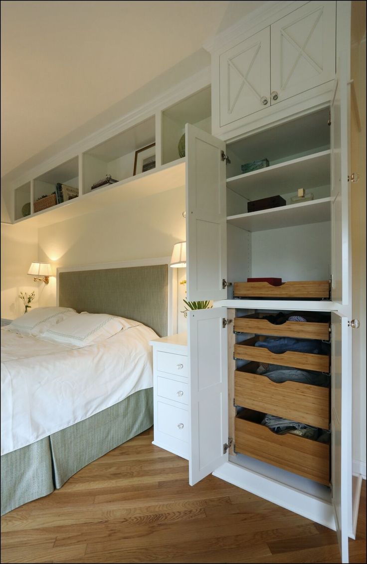 a bed sitting next to a white closet filled with drawers