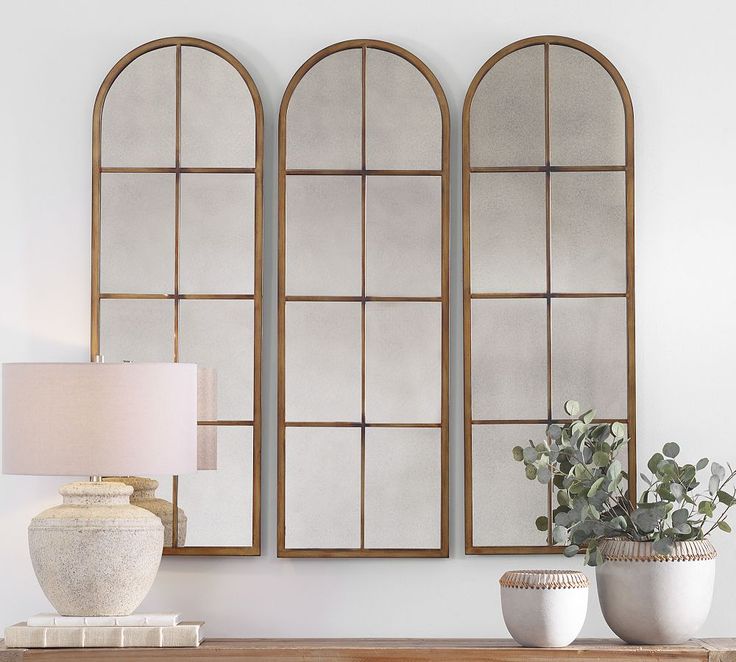 three mirrors on the wall above a table with two vases and a lamp next to it