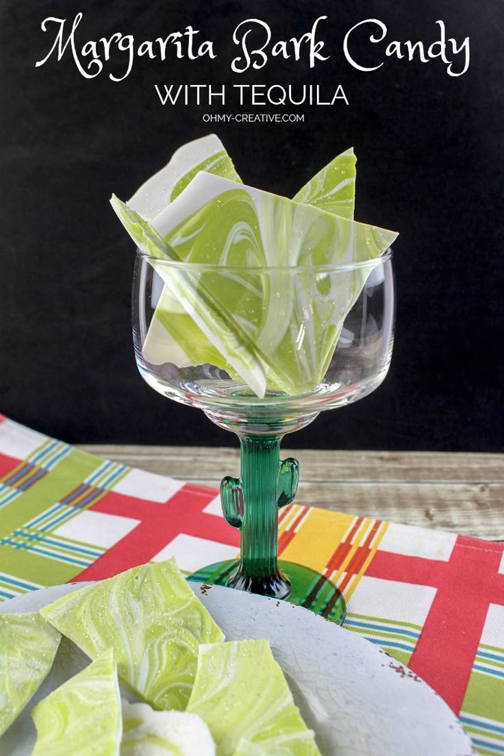 a green glass filled with candy sitting on top of a table next to some pieces of paper