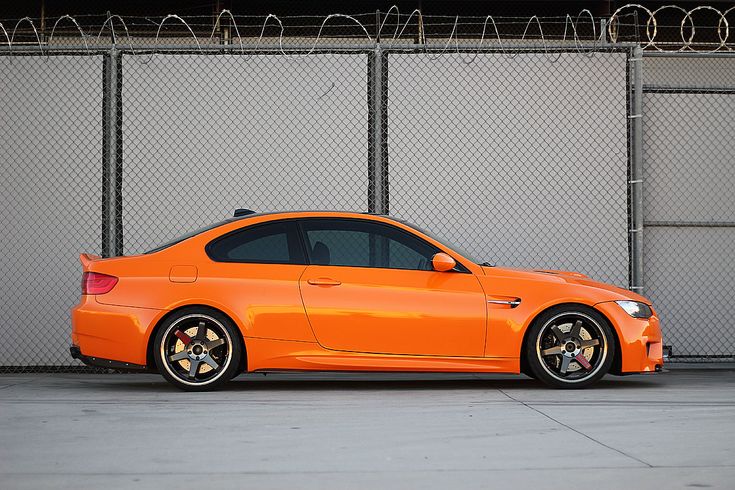 an orange car parked in front of a fence