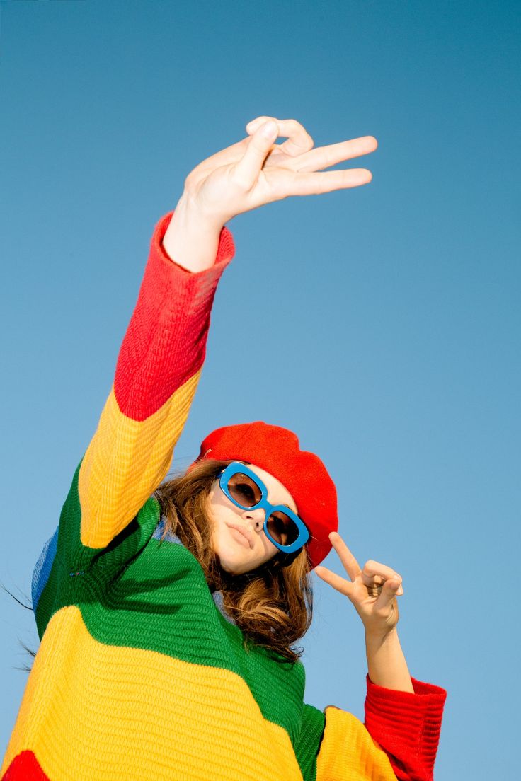 a woman wearing sunglasses and a colorful sweater is holding her hand up in the air